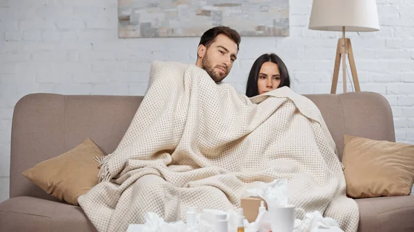 Sick couple under blanket in living room - foto de stock