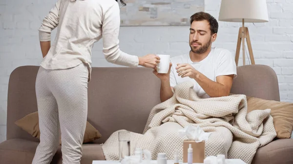 Caring woman giving cup of tea to sick man in living room — Fotografia de Stock