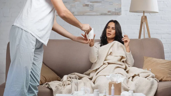 Caring man giving cup of tea to sick girlfriend in living room — Stock Photo