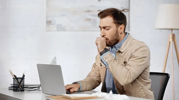 Allergic businessman couching near laptop on desk - foto de stock