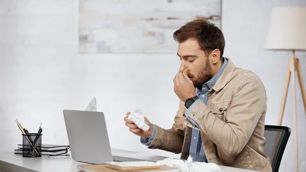 Allergic businessman with running nose sneezing near laptop on desk — Stock Photo