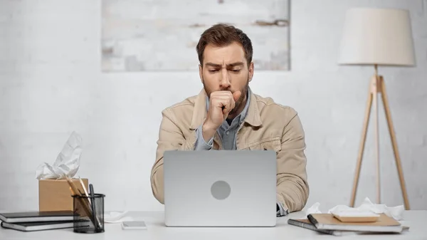 Allergic businessman couching near laptop and smartphone on desk - foto de stock