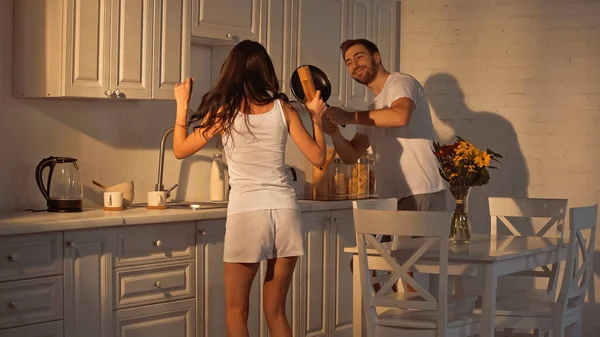 Happy man with frying pan dancing near girlfriend with paper mill — Stock Photo