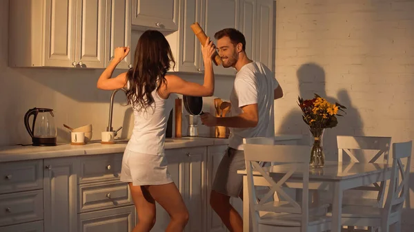 Fröhlicher Mann mit Bratpfanne tanzt neben Freundin mit Papiermühle — Stockfoto