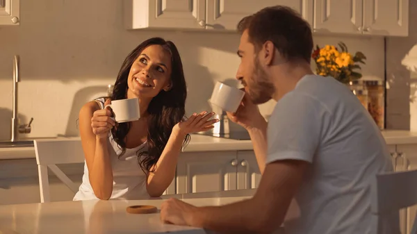 Happy young woman holding cup of coffee and talking with blurred boyfriend — Fotografia de Stock