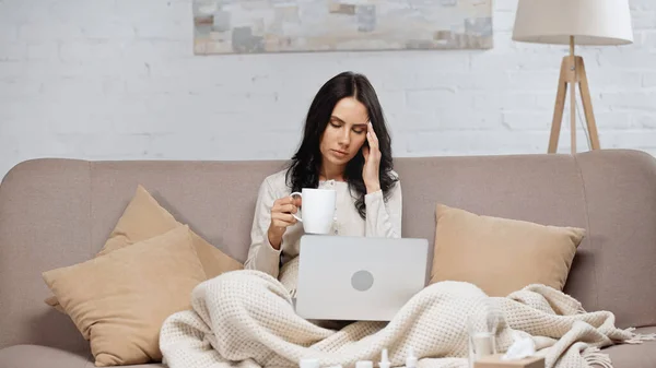 Sick freelancer holding cup of tea while suffering from headache — Stock Photo
