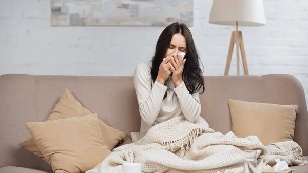 Sick brunette woman with running nose sitting on sofa with tissue — Photo de stock