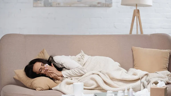 Kranke brünette Frau mit rennender Nase auf Sofa liegend mit Gewebe — Stockfoto
