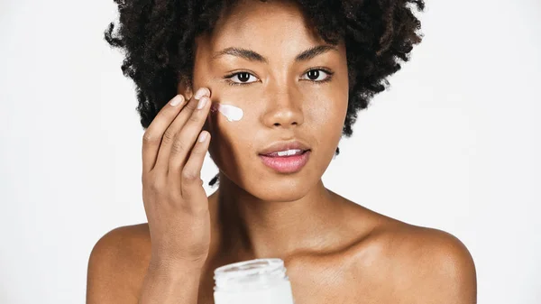 Giovane donna afroamericana che applica crema sul viso isolata sul grigio — Foto stock