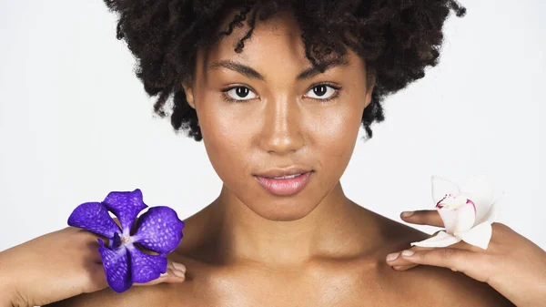 African american woman with perfect skin holding orchid flowers isolated on grey — Stock Photo