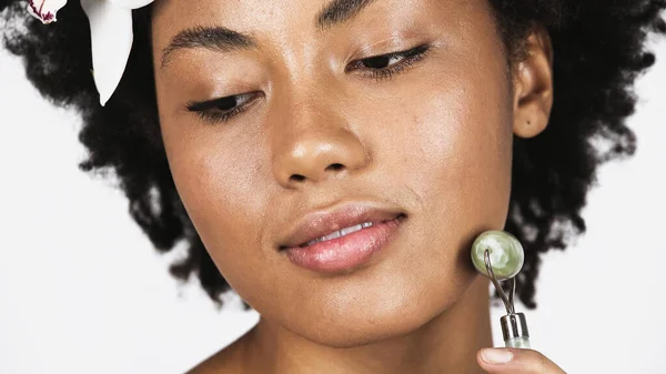 Nahaufnahme der afrikanisch-amerikanischen Frau mit Orchidee im Haar mit Jade-Rolle isoliert auf grau — Stockfoto