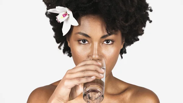 African american woman with orchid in hair drinking water isolated on grey — Stock Photo