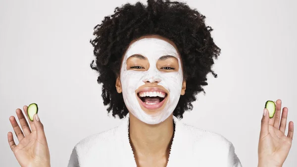Mulher americana africana alegre em máscara facial segurando fatias de pepino isolado em cinza — Fotografia de Stock