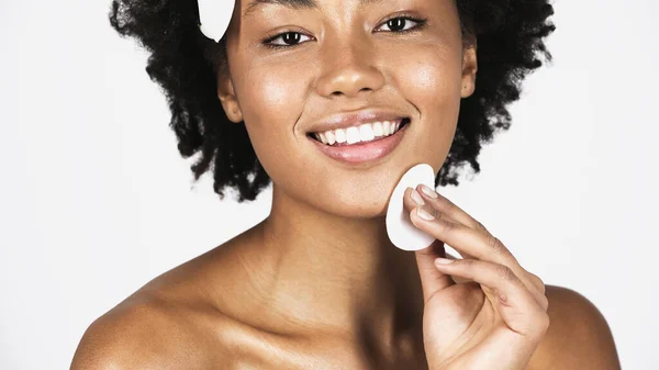 Sorrindo afro-americana limpeza rosto com almofada de algodão isolado em cinza — Fotografia de Stock