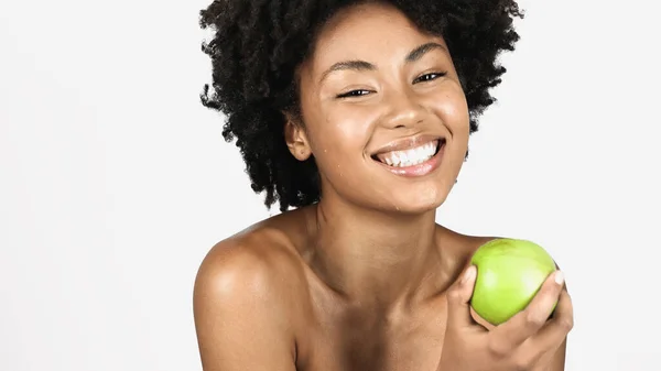 Mujer afroamericana positiva con hombros desnudos sosteniendo jugosa manzana verde aislada en gris - foto de stock