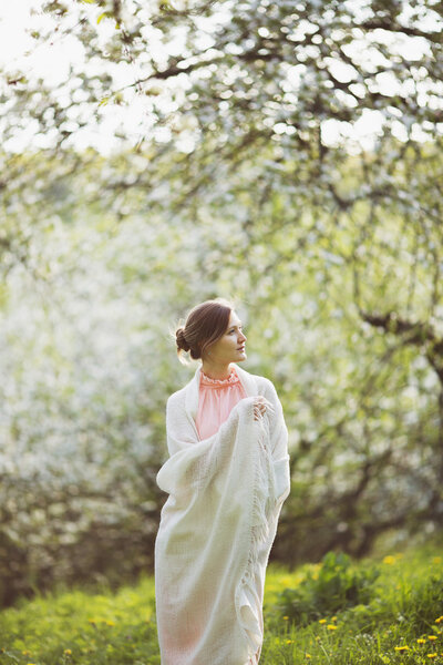 Happy young woman stands in the middle of a blossoming garden