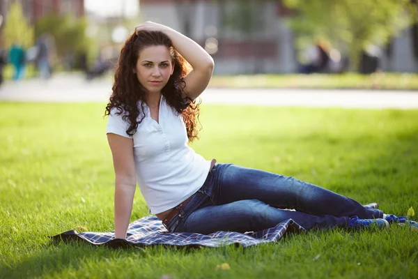 Mulher bonita em jeans senta-se na grama — Fotografia de Stock