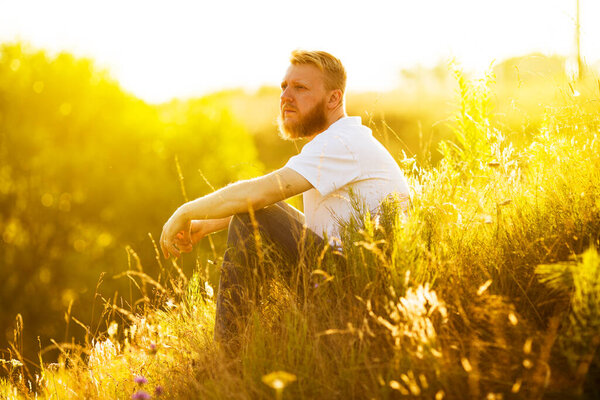 Бородач сидит на траве и смотрит вдаль