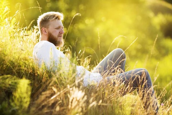 Young man with a beard lies on a summer meadow