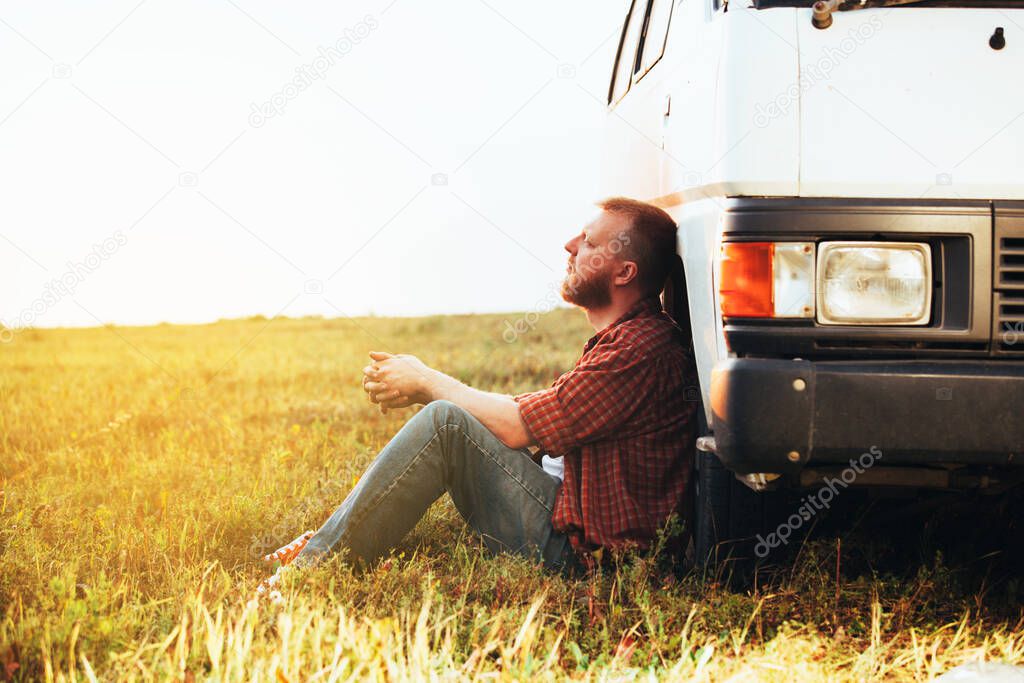 Bearded driver in a shirt and jeans sits near his car