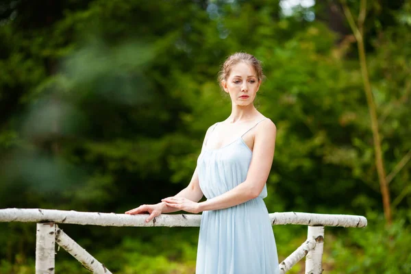 橋の上に長い青いドレスの美しい若い女性が立っている — ストック写真