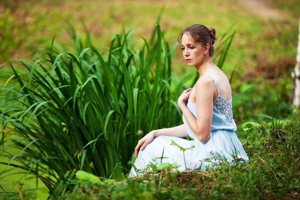 身穿蓝色衣服的漂亮女人坐在湖边的草地上 — 图库照片