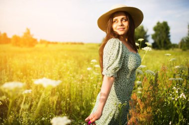 Şapkalı genç bir kadın çiçek tarlasında yürüyor.