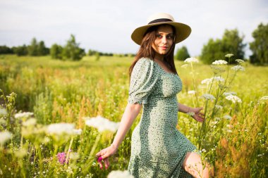 Şapkalı, uzun saçlı, tarlada yürüyen mutlu genç bir kadın.