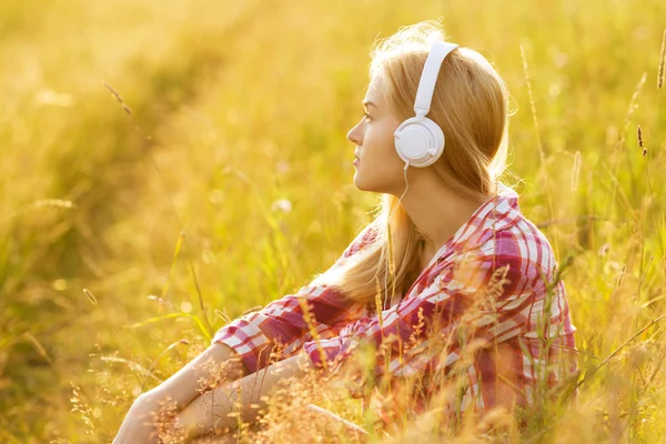 Dívka se sluchátky na uších sedí v trávě — Stock fotografie