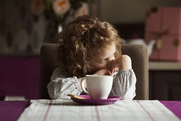 Pequena menina de cabelos encaracolados sentada à mesa Imagens Royalty-Free