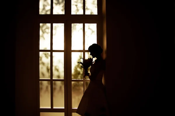 Noiva com um buquê de pé na janela — Fotografia de Stock