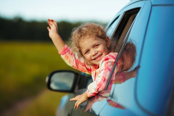 Happy little girl waving from the car — Stock Photo, Image