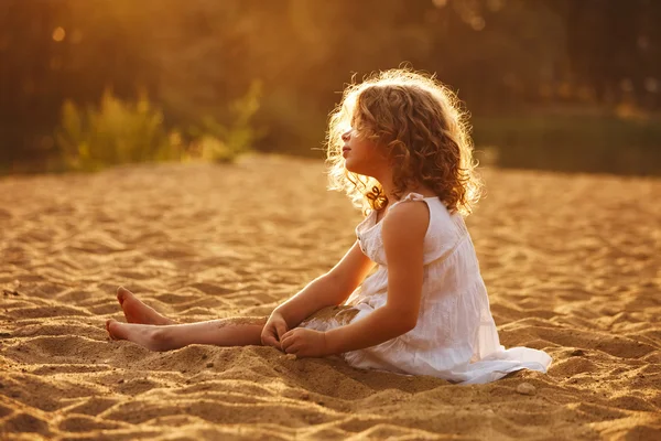 Little girl in dress sitting on the sand — Stock Photo, Image