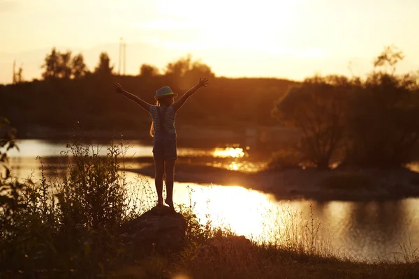 Mädchen steht bei Sonnenuntergang am Fluss — Stockfoto