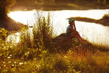 Nehir kıyısında oturan şapkalı kız
