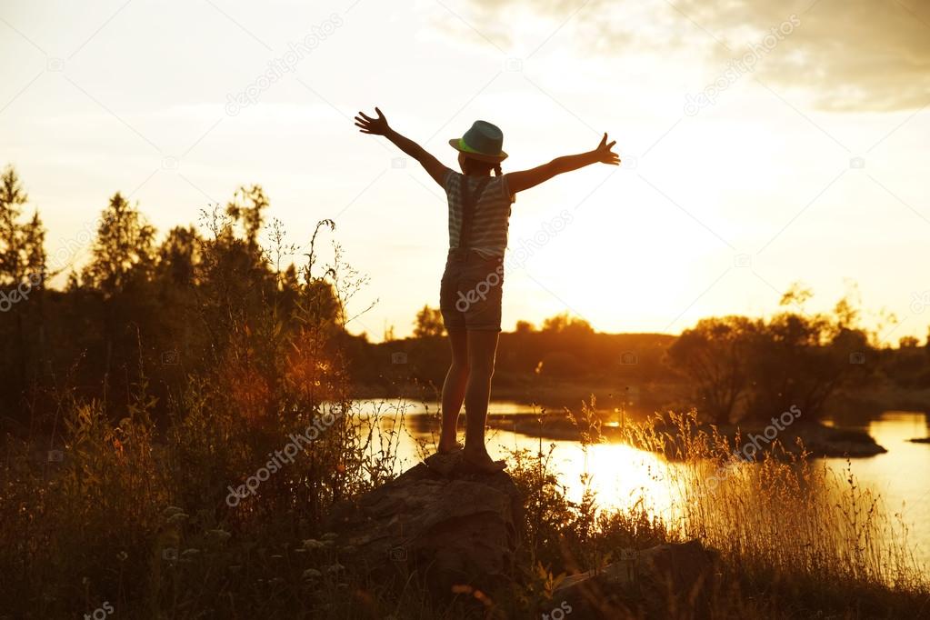 Happy girl standing on a rock at sunset