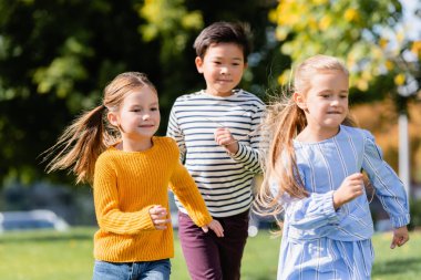 Parkta etnik çeşitlilikte arkadaşların yanında koşan gülen kız 
