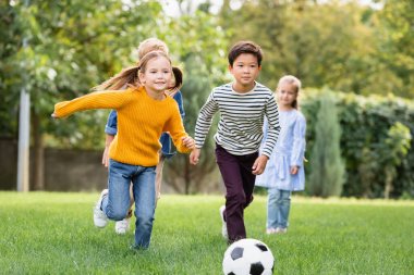 Parktaki bulanık arka planda futbol oynayan neşeli çoklu etnik çocuklar. 