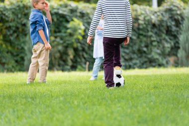 Çimenlerde futbol oynayan çocuk, bulanık arka planda arkadaşlarının yanında. 
