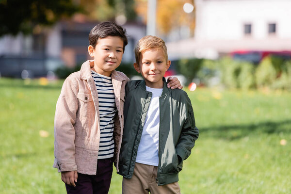 Улыбающийся азиатский мальчик обнимает друга в парке 