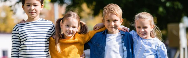 Alegres Niños Multiétnicos Abrazándose Mientras Miran Cámara Aire Libre Pancarta — Foto de Stock