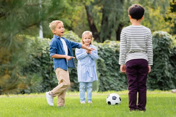 Spännande Pojke Pekar Med Fingrarna Nära Fotboll Och Vänner Parken — Stockfoto