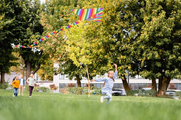 Kind Loopt Met Vliegende Vlieger Buurt Van Vrienden Wazige Achtergrond — Stockfoto