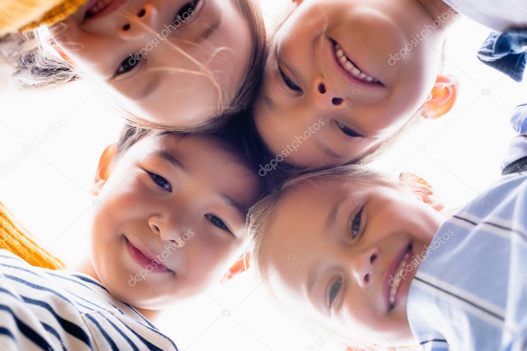 Bottom view of multiethnic kids smiling at camera isolated on white 