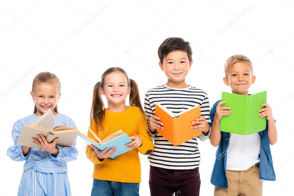 Multiethnic kids holding books while smiling at camera isolated on white
