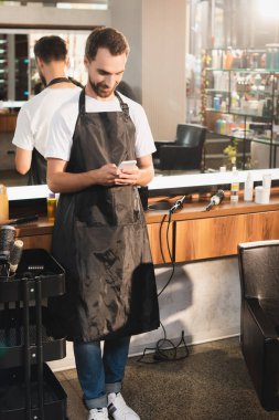 Genç berber aynanın yanındaki iş yerinde cep telefonuyla sohbet ediyor.