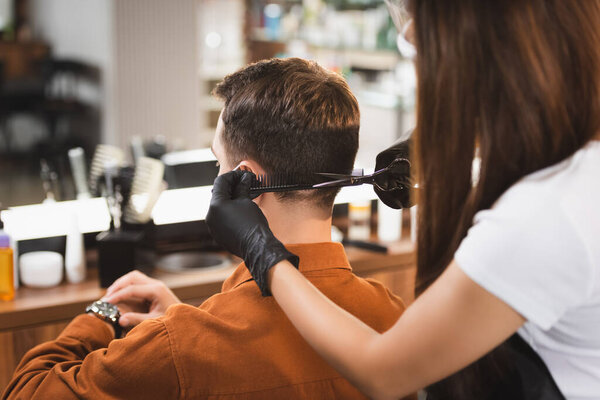 man looking at wristwatch while hairstylist on blurred foreground cutting his hair
