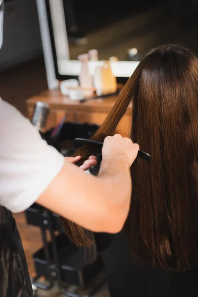 发型师在模糊的前景上梳理女人的头发 — 图库照片