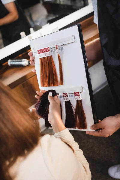 发型师将发色调色板放在客户端附近 在模糊的前景上触摸样品的剪裁视图 — 图库照片