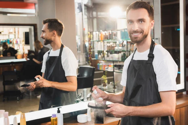 Χαμογελαστός Κομμωτής Απολύμανση Χτένα Απολυμαντικό Ενώ Στέκεται Κοντά Στον Καθρέφτη — Φωτογραφία Αρχείου